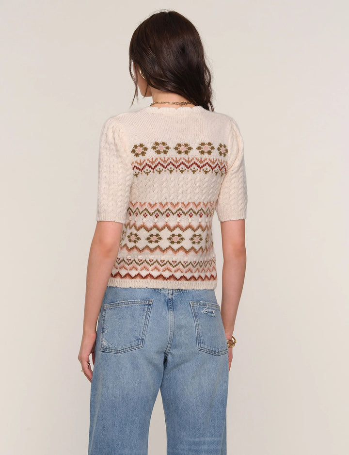 Person wearing a cream sweater with a patterned back and blue jeans on a plain background