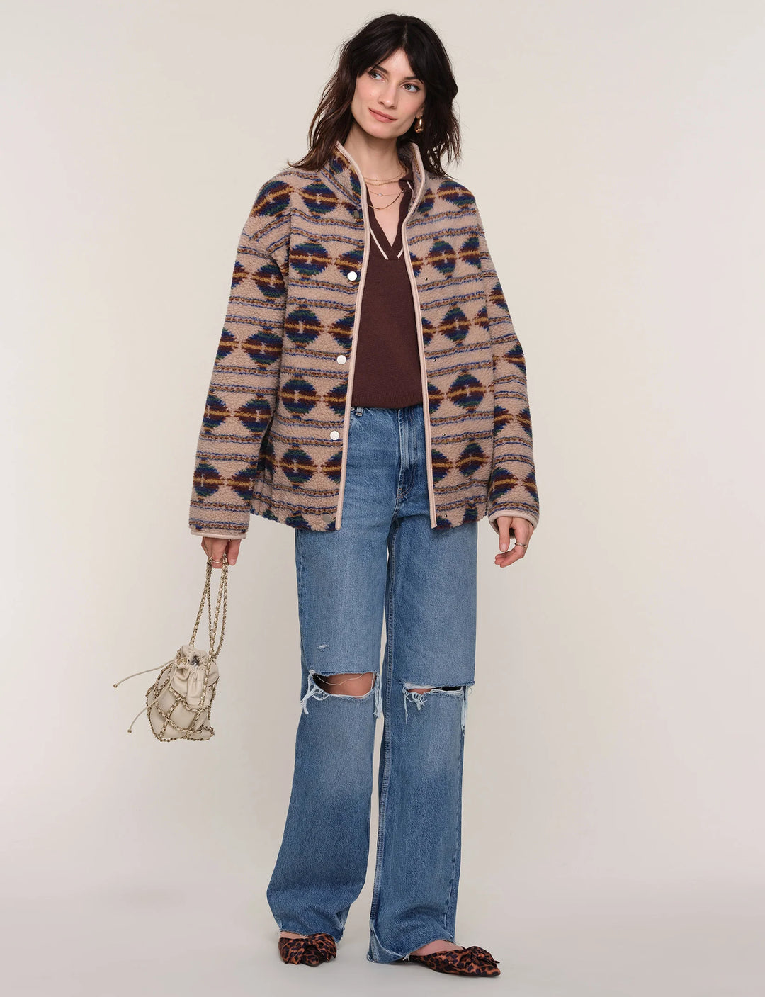 Woman wearing a patterned jacket and jeans on a plain background