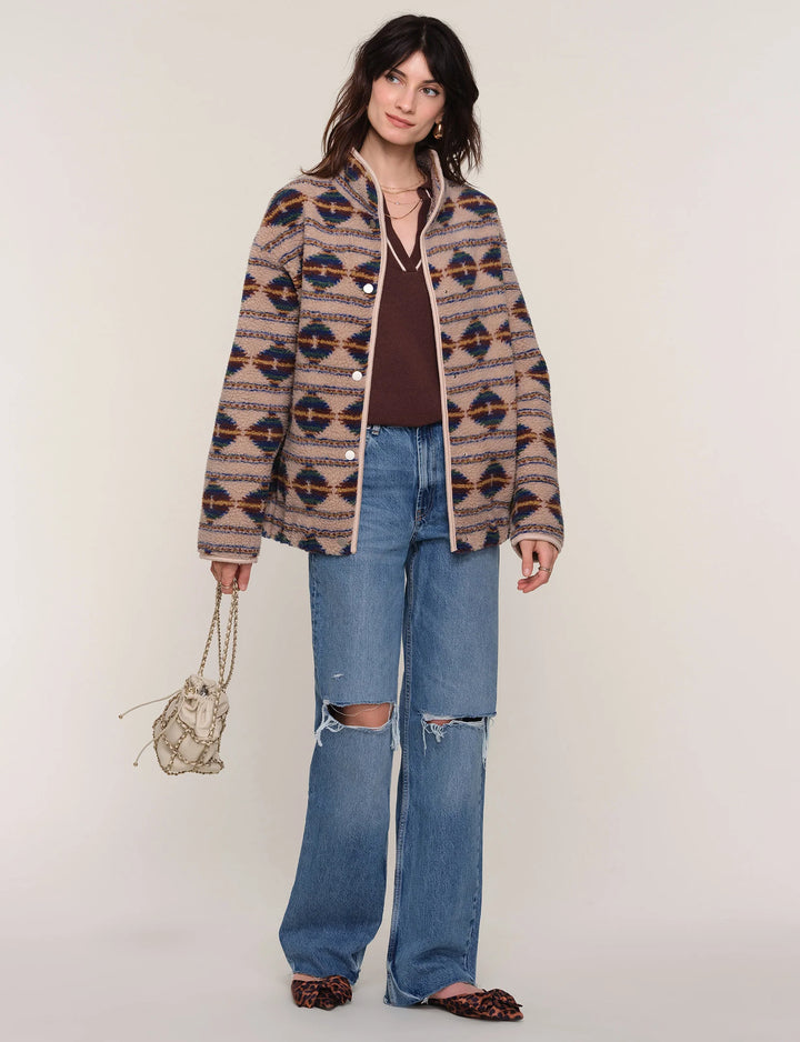 Woman wearing a patterned jacket and jeans on a plain background