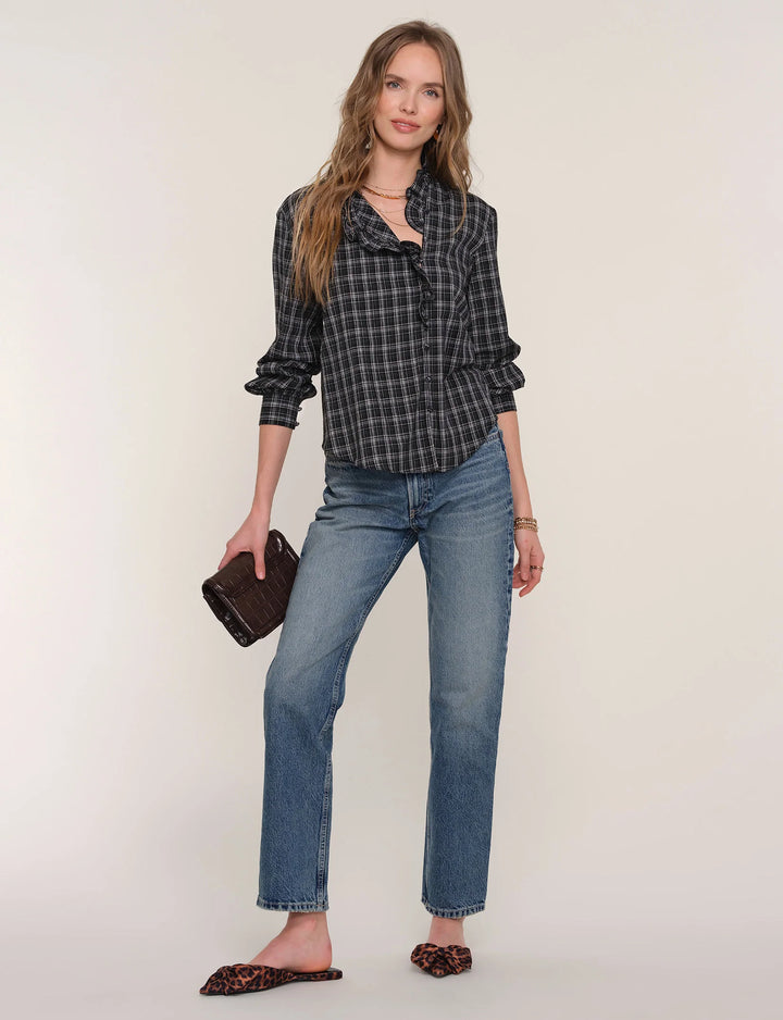 Woman wearing a plaid shirt and jeans with a brown clutch against a white background
