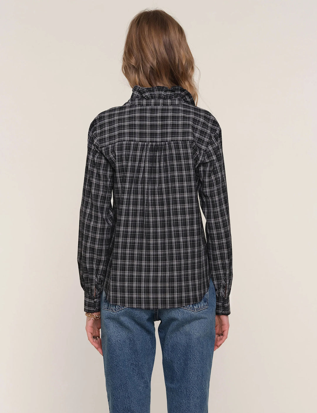 Person wearing a black and gray plaid shirt with blue jeans on a beige background
