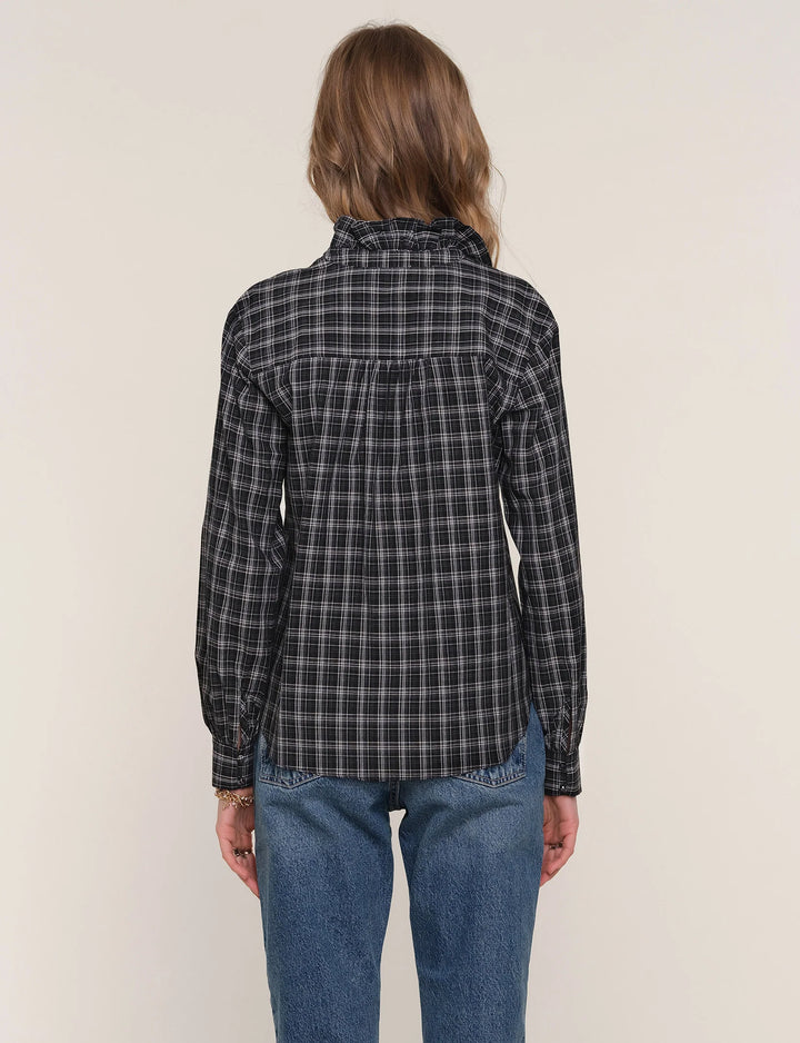 Person wearing a black and gray plaid shirt with blue jeans on a beige background