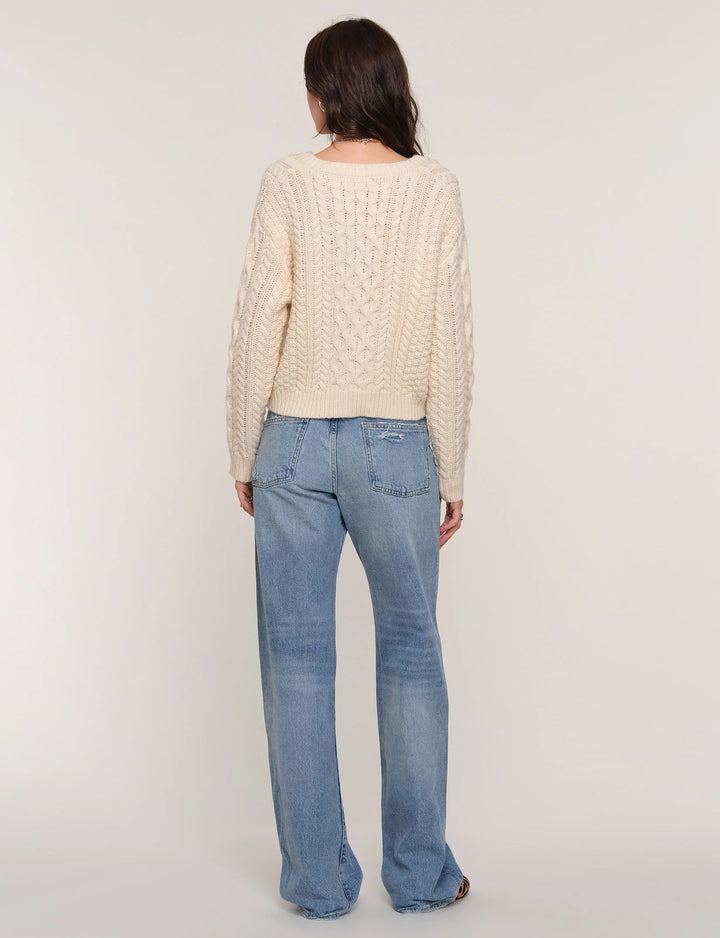 Person wearing a cream knitted sweater and blue jeans on a white background