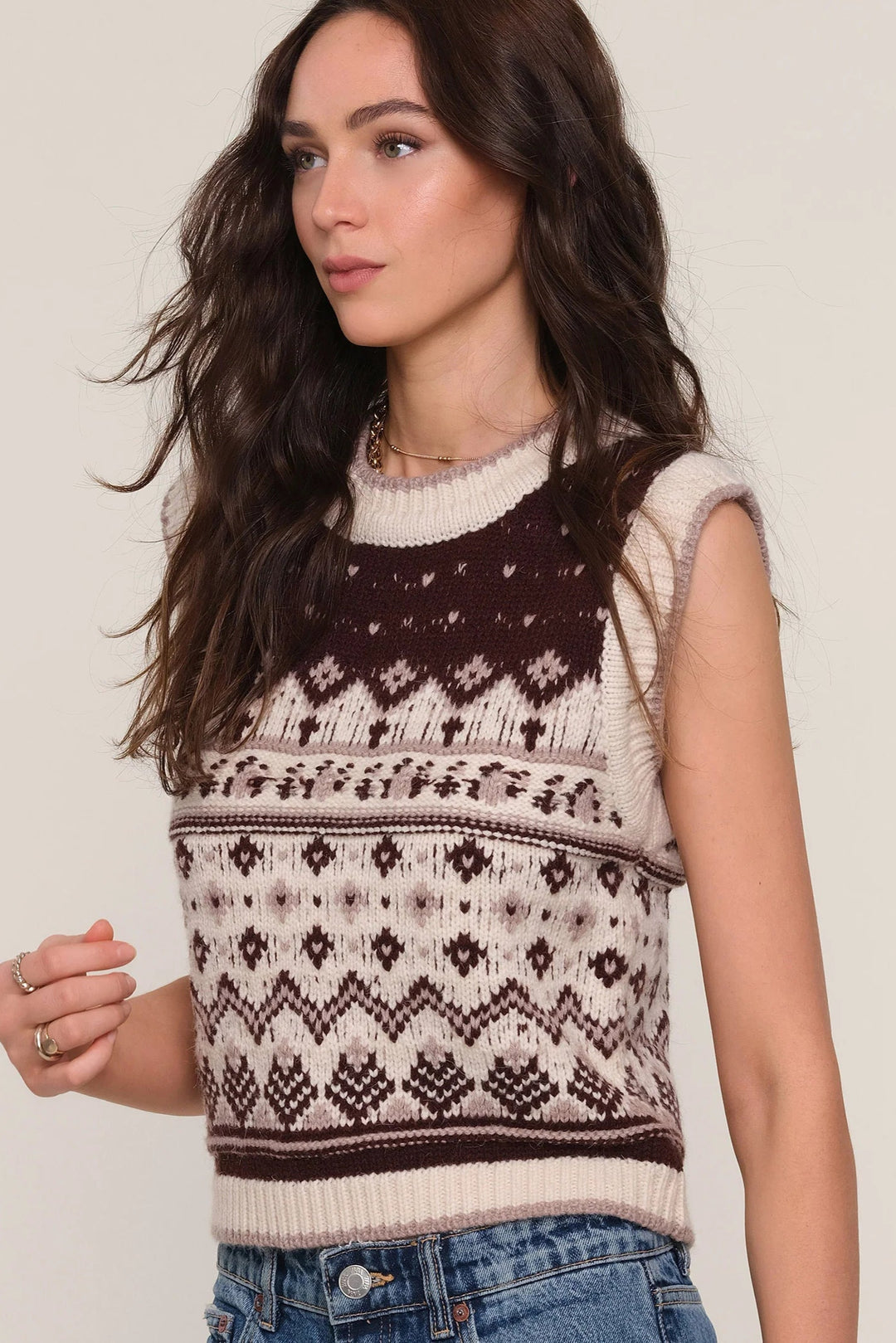 Woman wearing a sleeveless knitted sweater with a pattern against a plain background