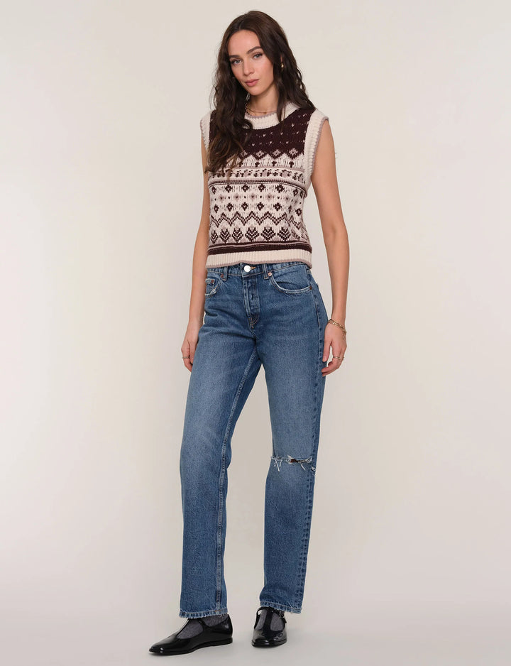 Woman wearing a patterned sleeveless top and blue jeans on a plain background