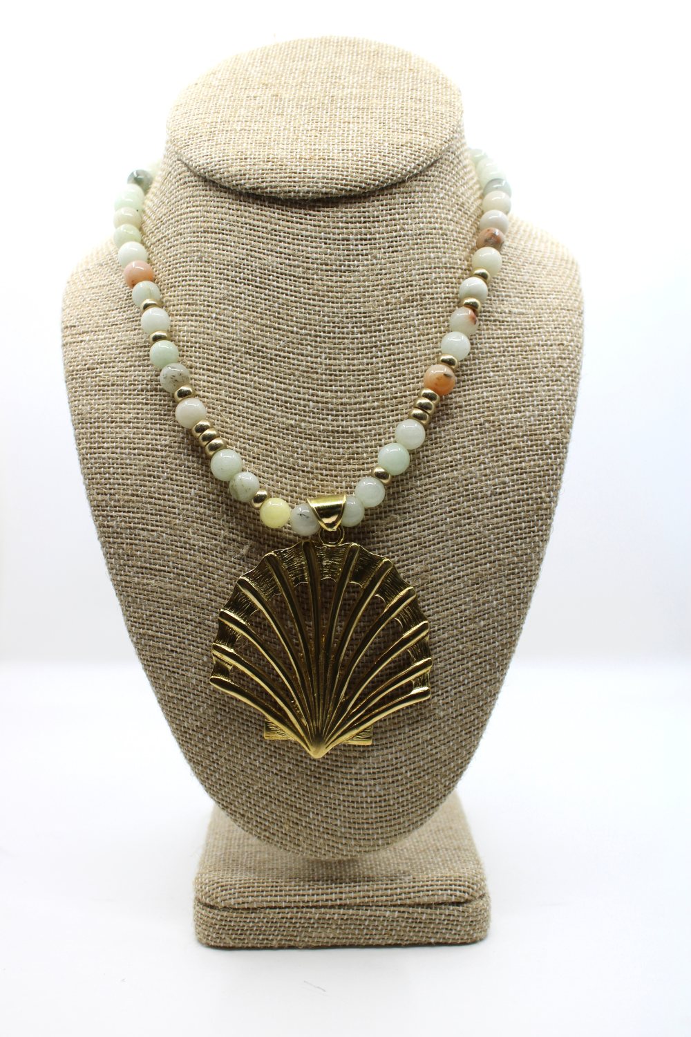 Necklace with a shell pendant on a beige bust against a white background