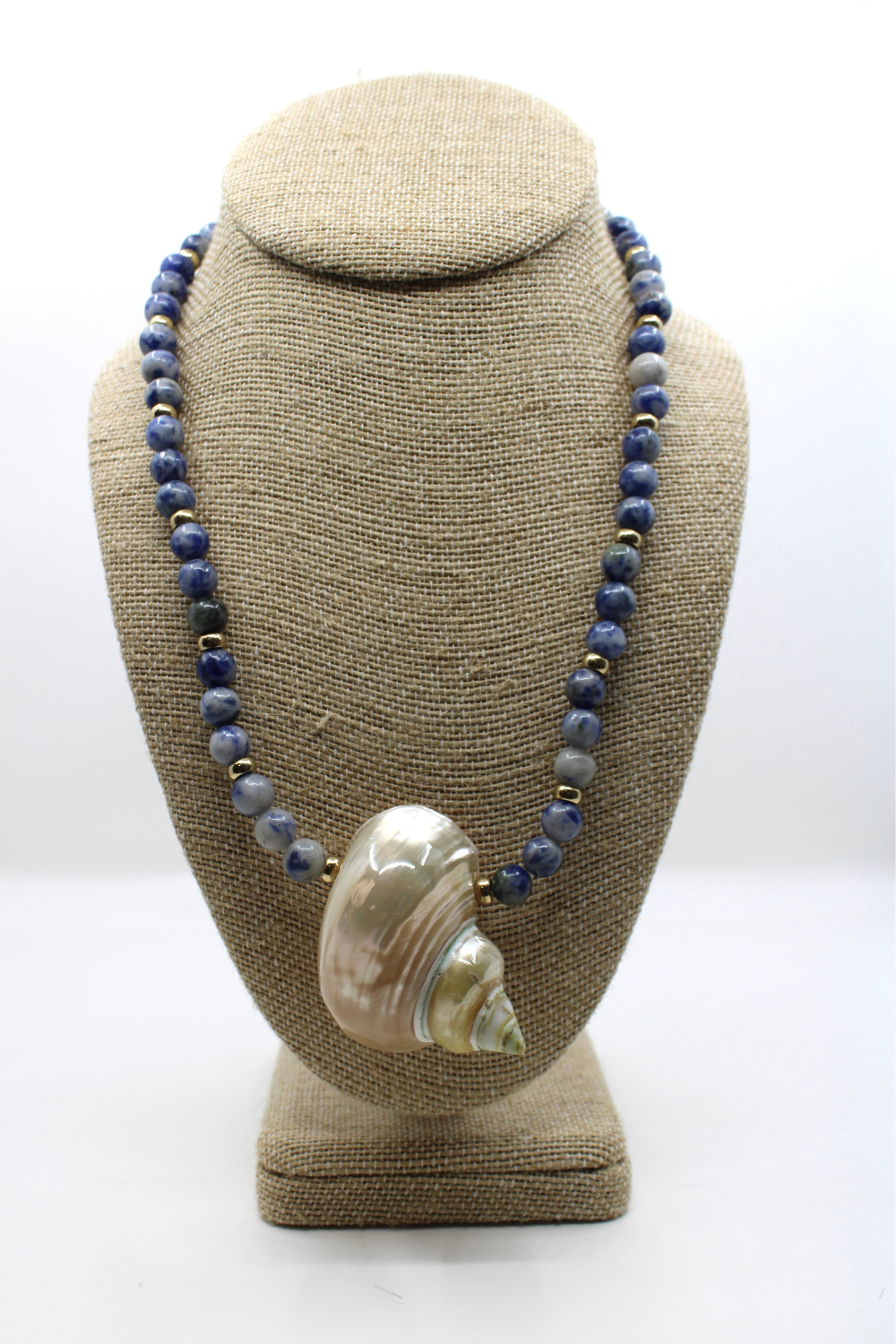 Necklace with shell pendant on a beige bust against a white background