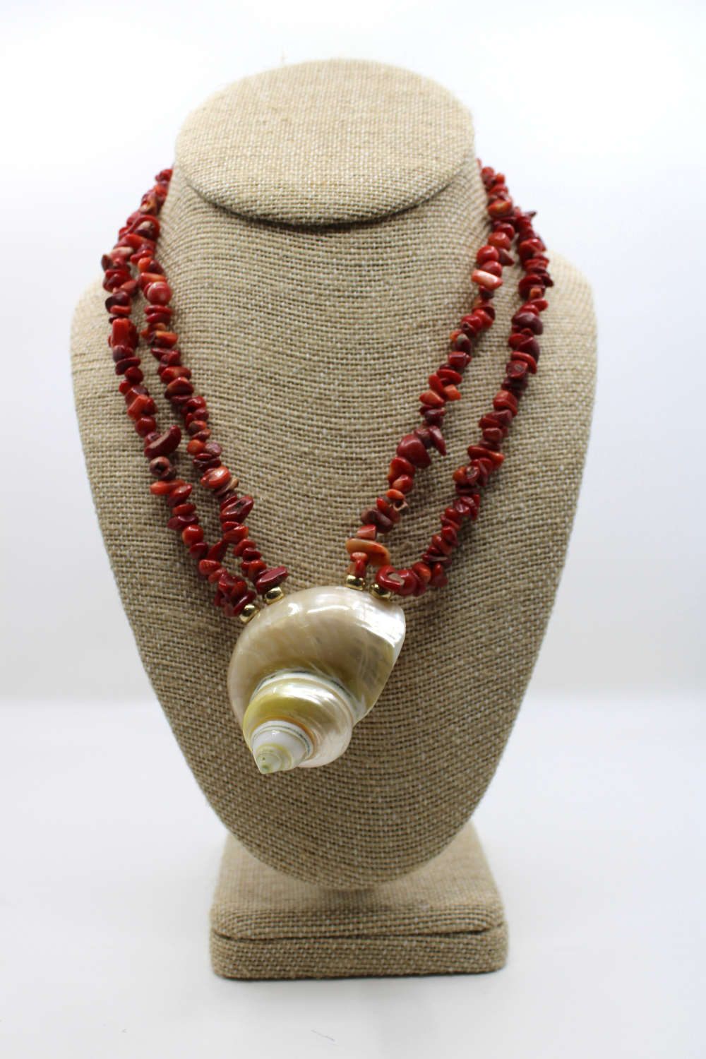 Necklace with red beads and a shell pendant on a beige bust against a white background