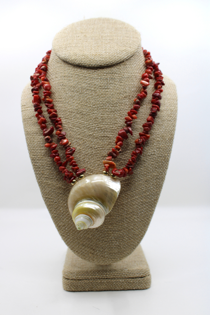 Necklace with red beads and a shell pendant on a beige bust against a white background