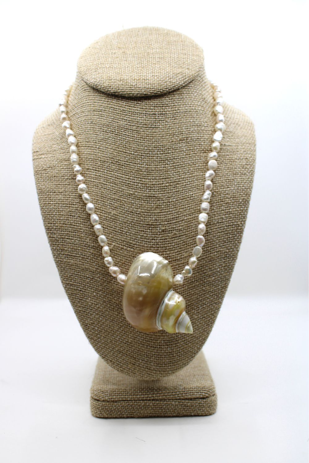 Necklace with a large shell pendant on a brown bust against a white background
