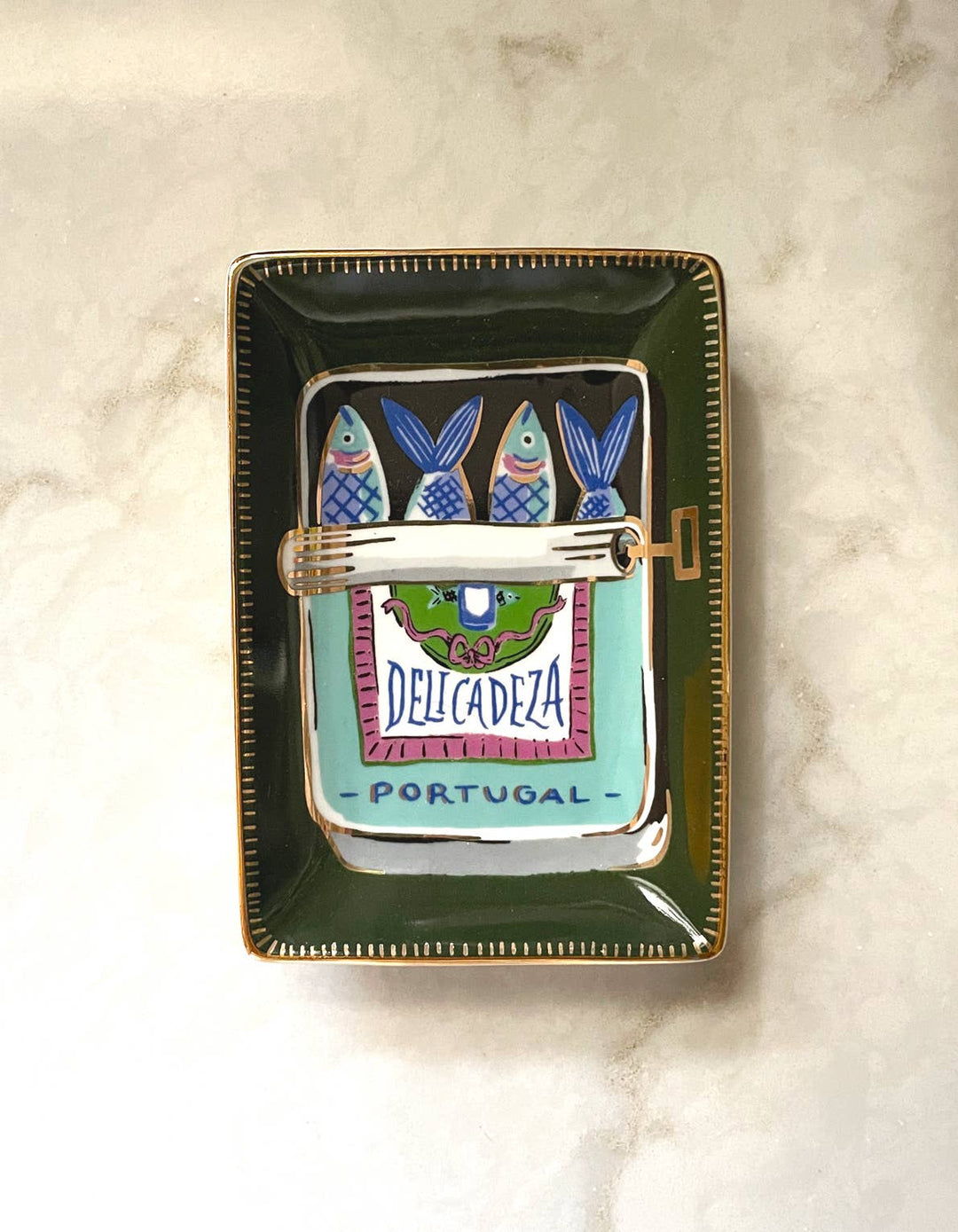 Decorative tray with a design of fish and 'Delicadeza Portugal' branding on a marble surface.