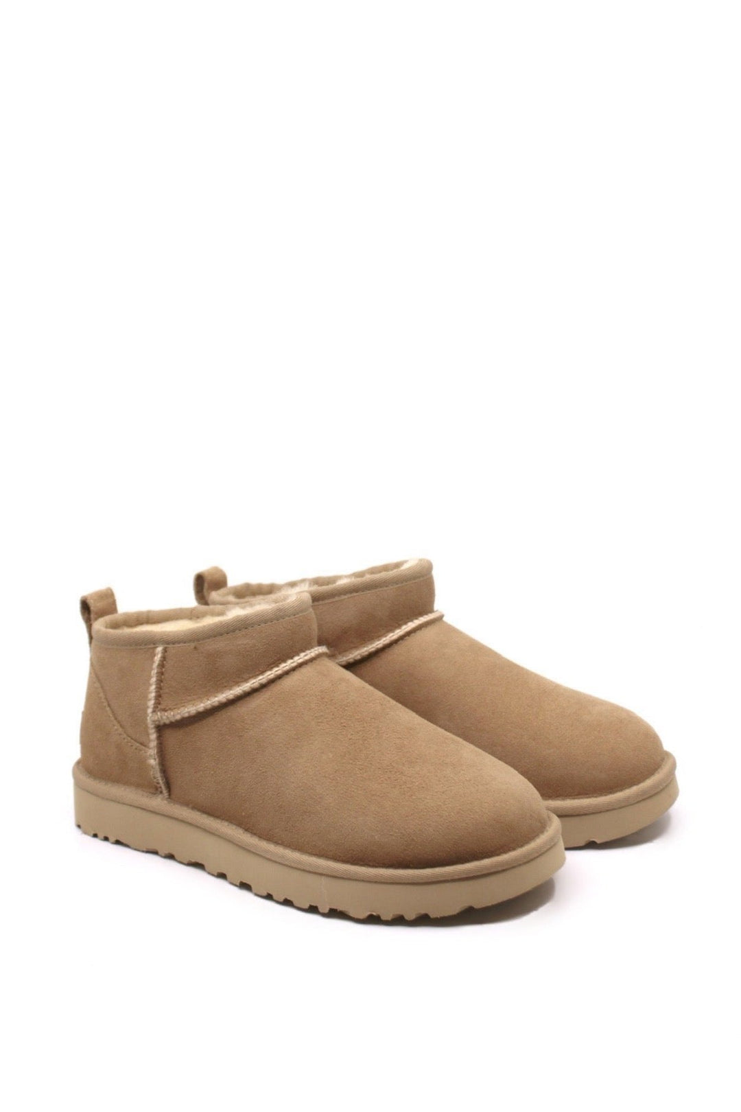 A pair of UGG Classic Ultra Mini boots in sand color, featuring an ankle height, shearling stuffing, and a round toe.
