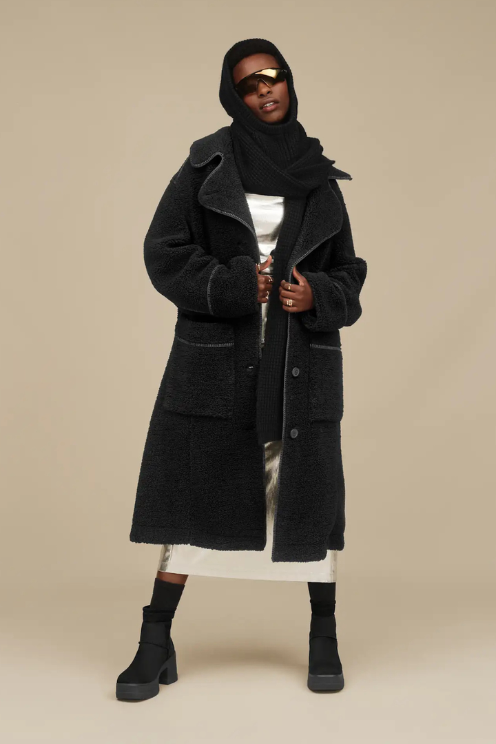 Person wearing a black coat, white dress, and black Chelsea boots from UGG 