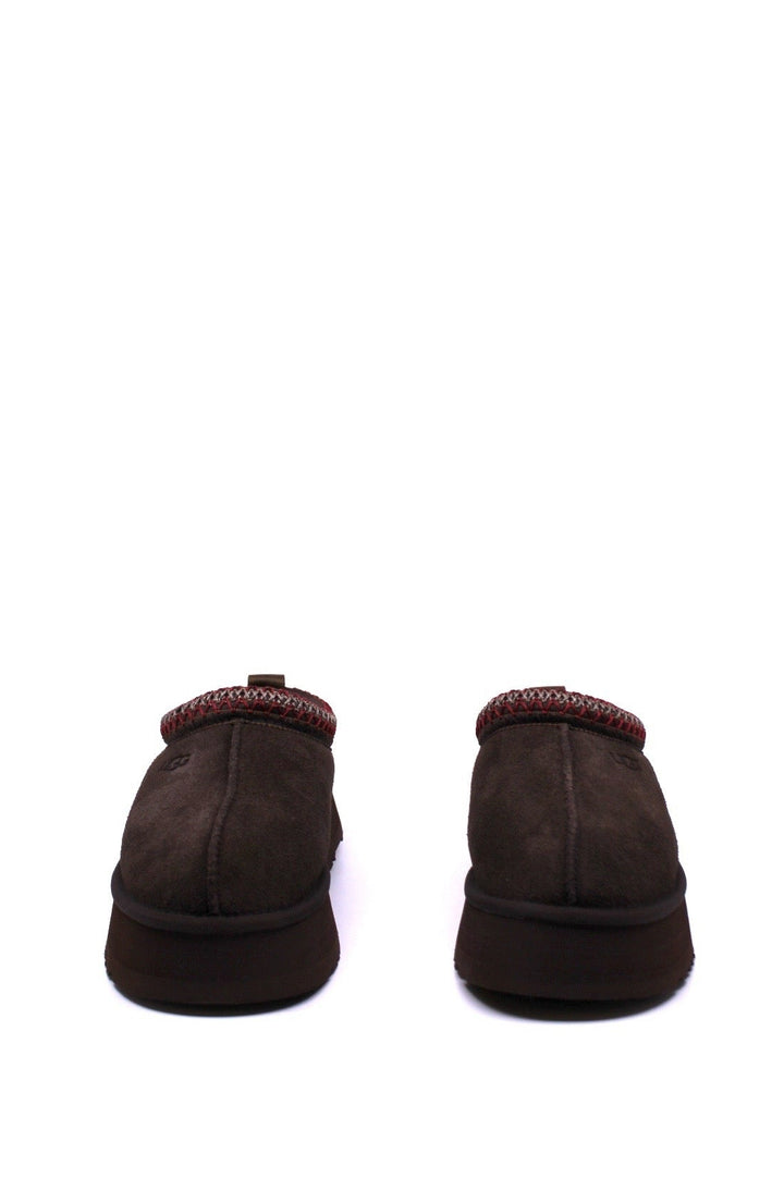Pair of brown UGG slippers with red trim on a white background