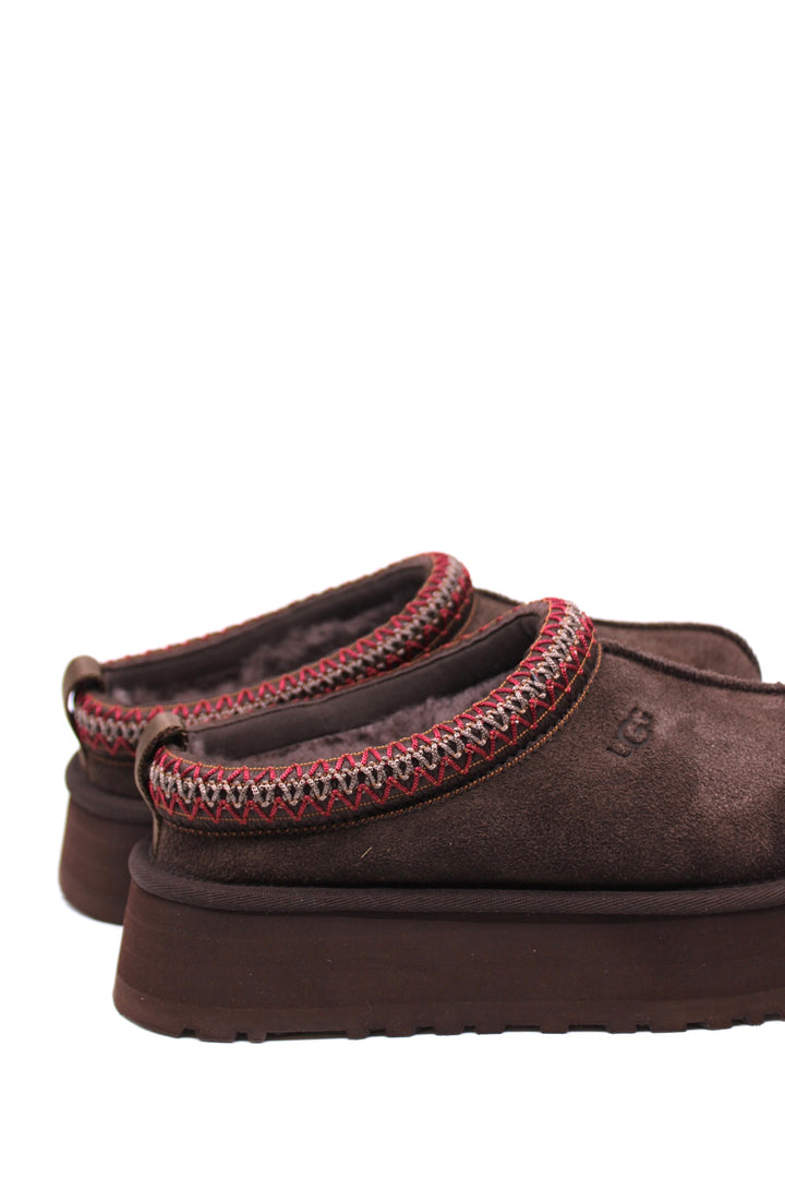 Pair of brown UGG slippers with red trim on a white background
