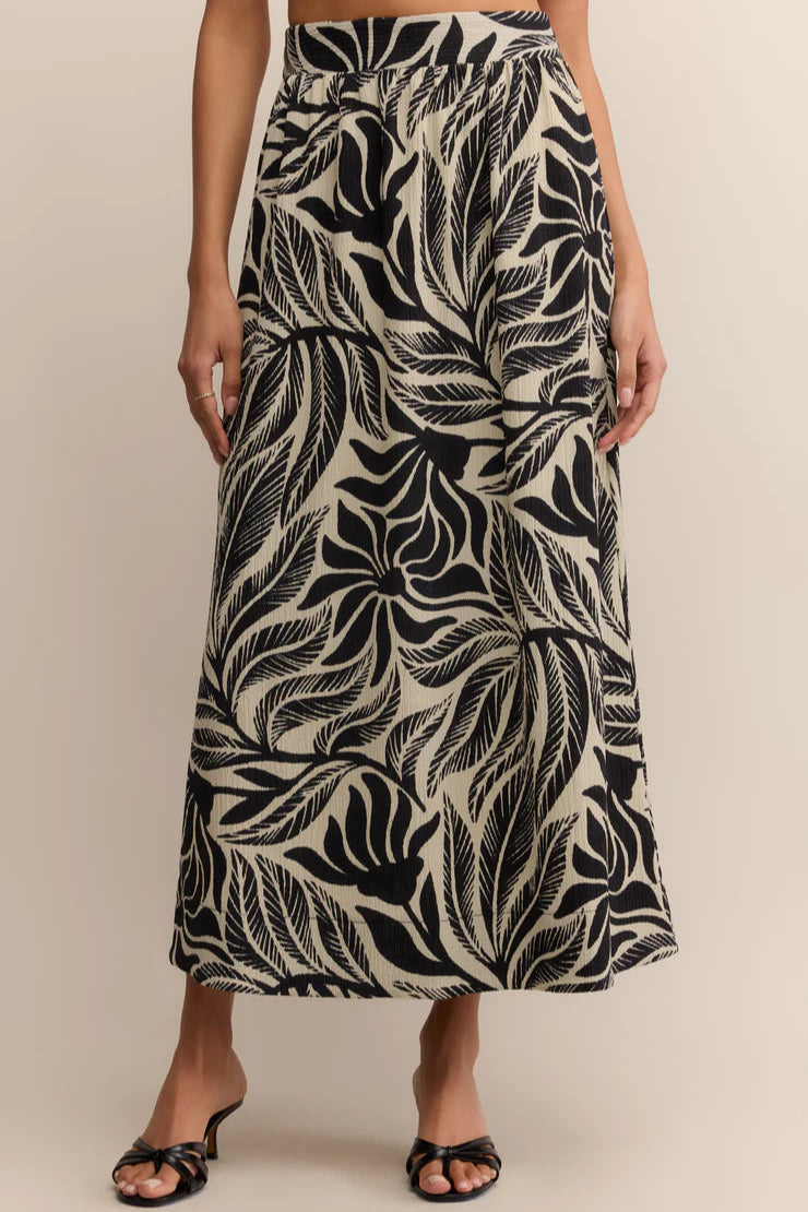 Person wearing a black and white leaf patterned skirt on a beige background