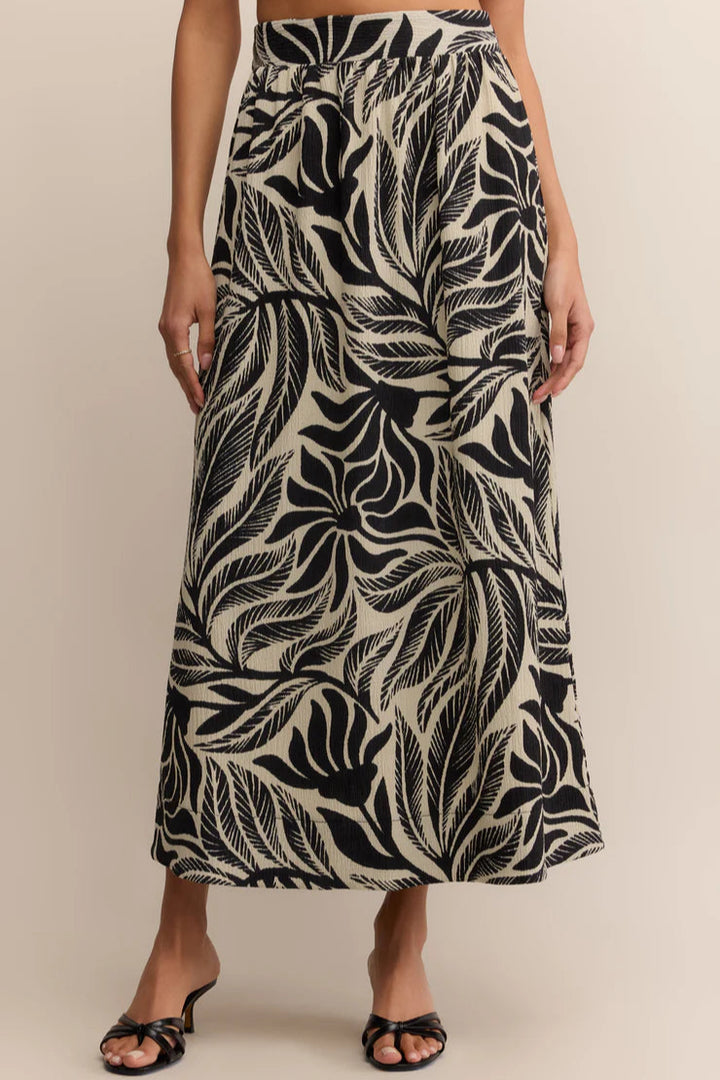 Person wearing a black and white leaf patterned skirt on a beige background