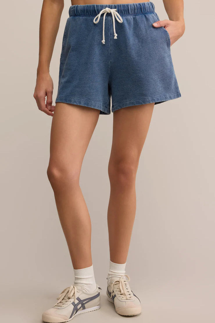 Person wearing blue denim shorts and white sneakers on a beige background
