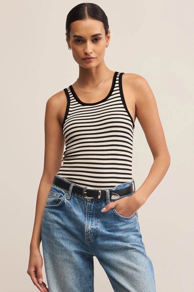 Woman wearing a black and white striped tank top and blue jeans on a beige background