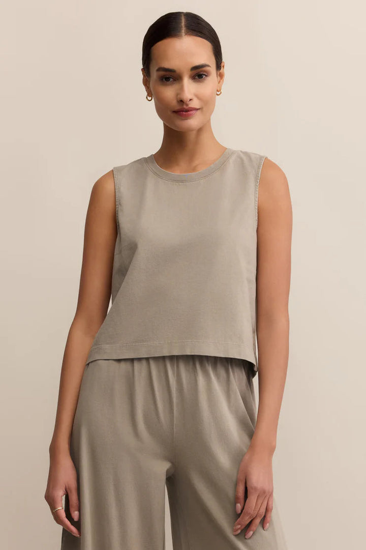 Woman wearing a beige sleeveless top and pants against a beige background
