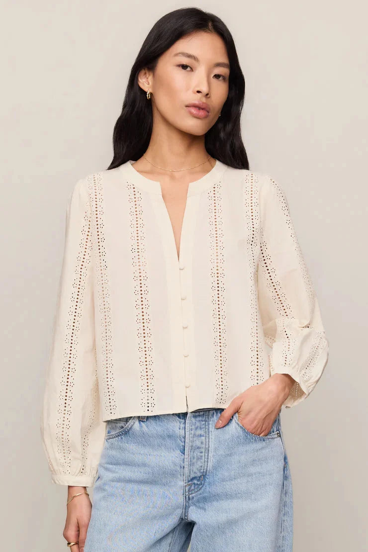 Woman wearing a cream blouse and light blue jeans against a plain background