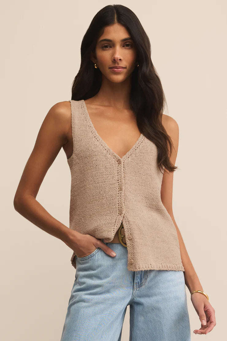 Woman wearing a beige knitted vest and light blue jeans against a beige background