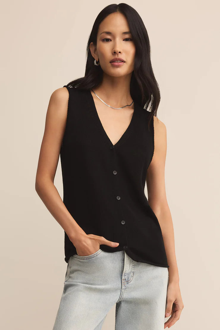 Woman wearing a black sleeveless top and light blue jeans against a beige background