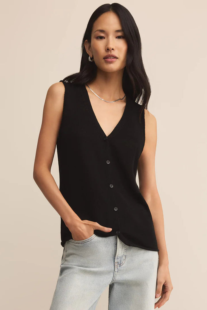 Woman wearing a black sleeveless top and light blue jeans against a beige background