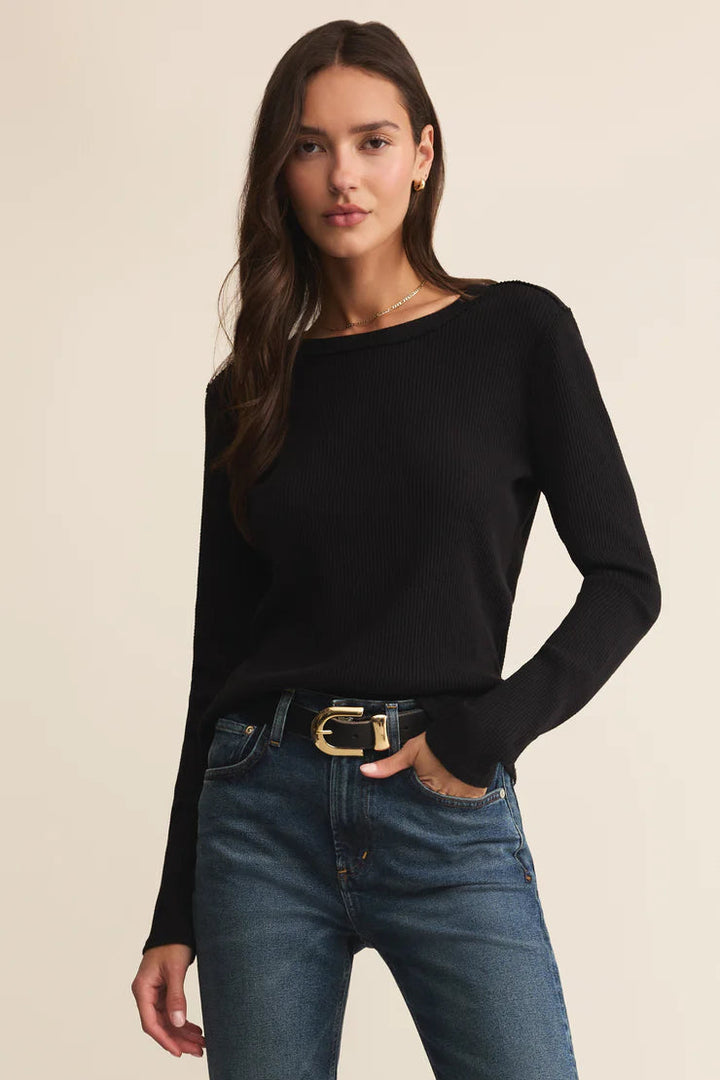Woman wearing a black long-sleeve top and blue jeans on a beige background
