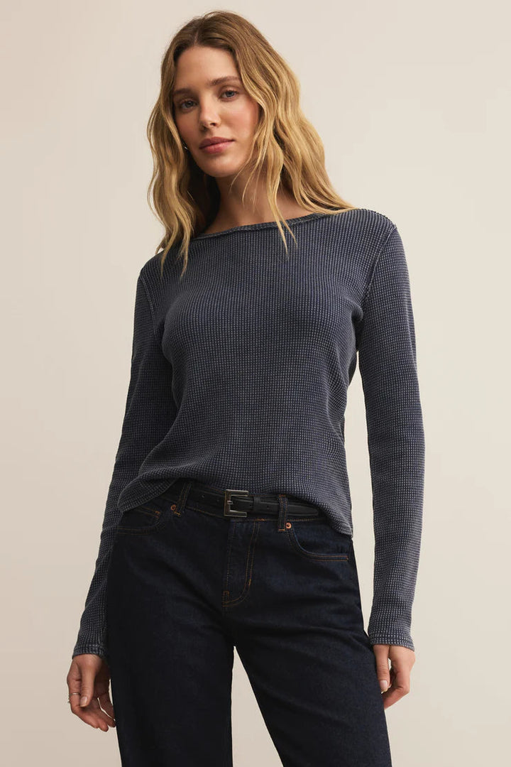 Woman wearing a blue ribbed sweater and dark jeans against a beige background