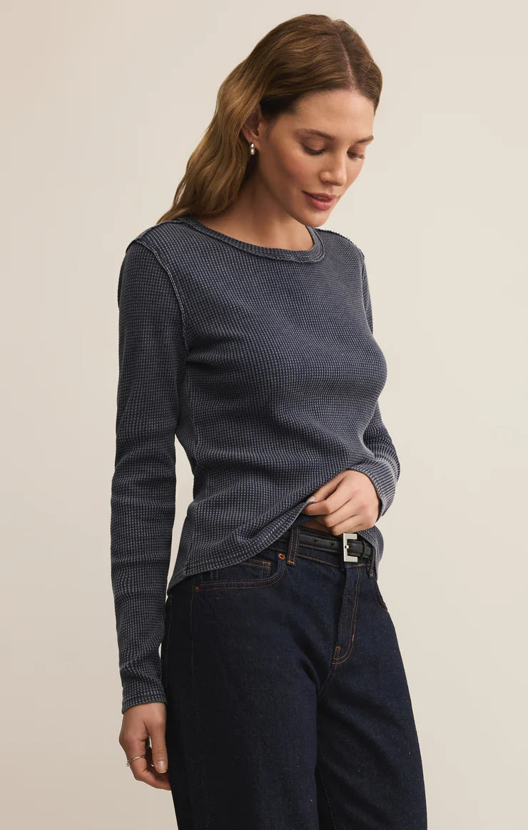 Woman wearing a blue textured sweater and dark jeans on a plain background