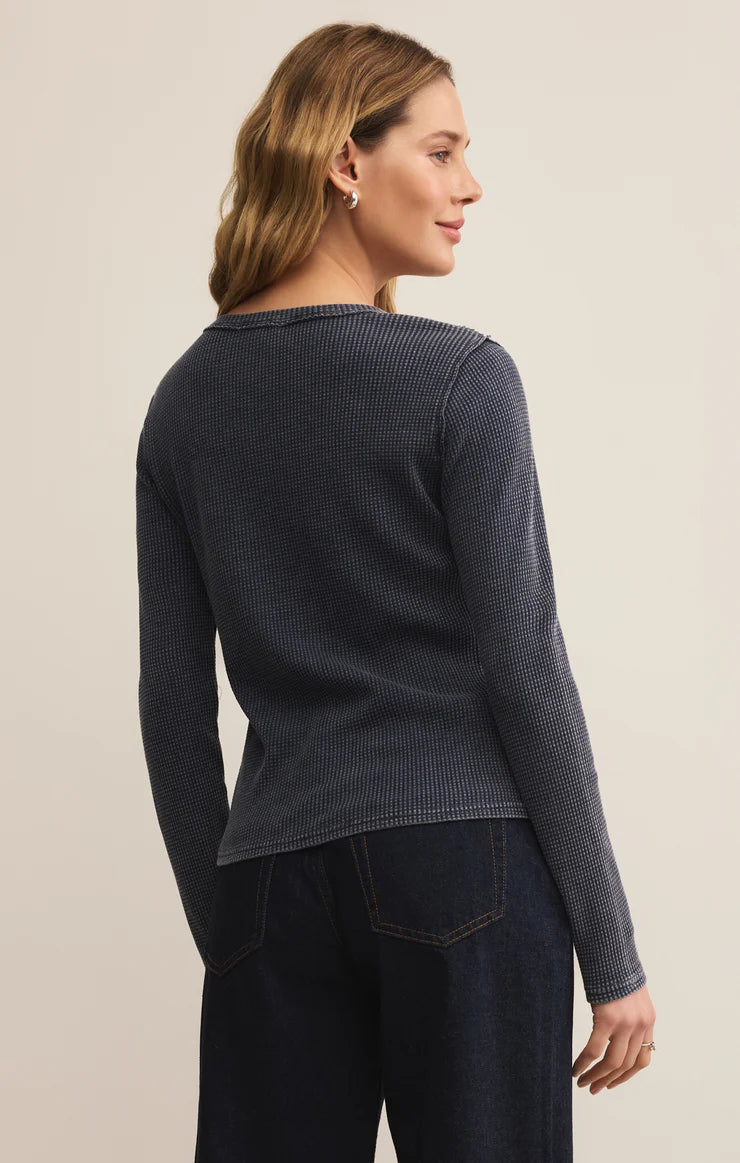 Woman wearing a navy blue sweater and dark jeans against a beige background