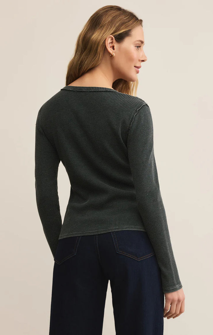 Woman wearing a dark green sweater and dark blue pants on a beige background