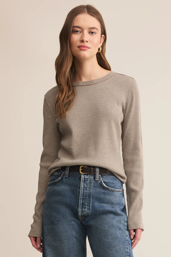 Woman wearing a beige sweater and blue jeans on a beige background