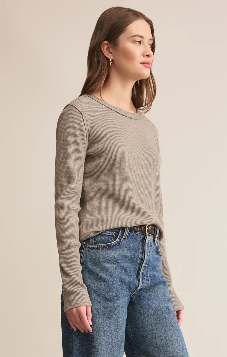 Woman wearing a beige sweater and blue jeans on a plain background