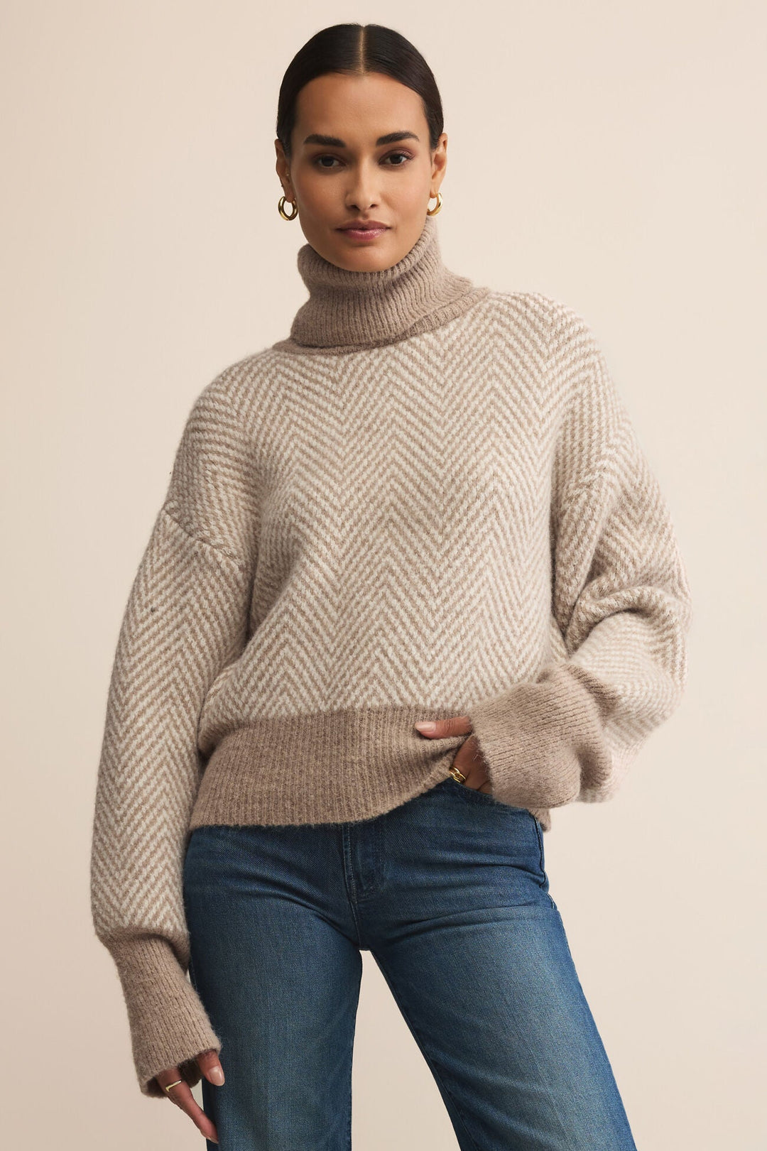 Woman wearing a beige sweater and blue jeans against a beige background