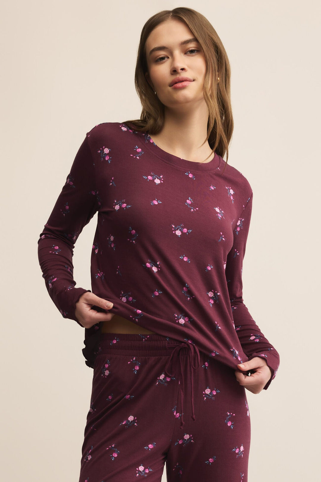 Woman wearing a maroon long-sleeve top and pants with a subtle pattern on a beige background