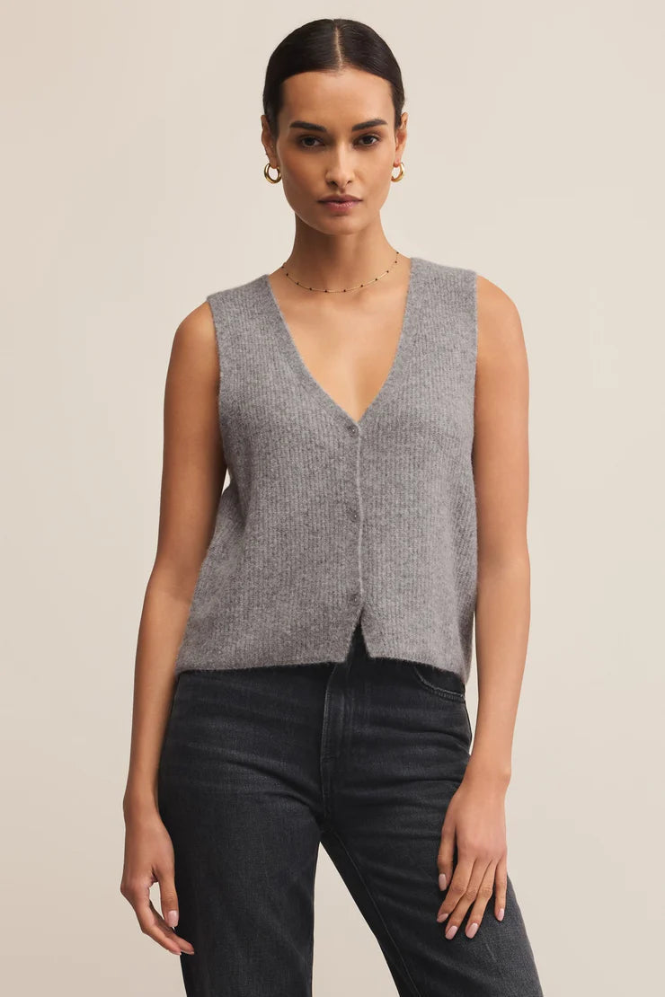 Woman wearing a gray sleeveless sweater vest against a beige background