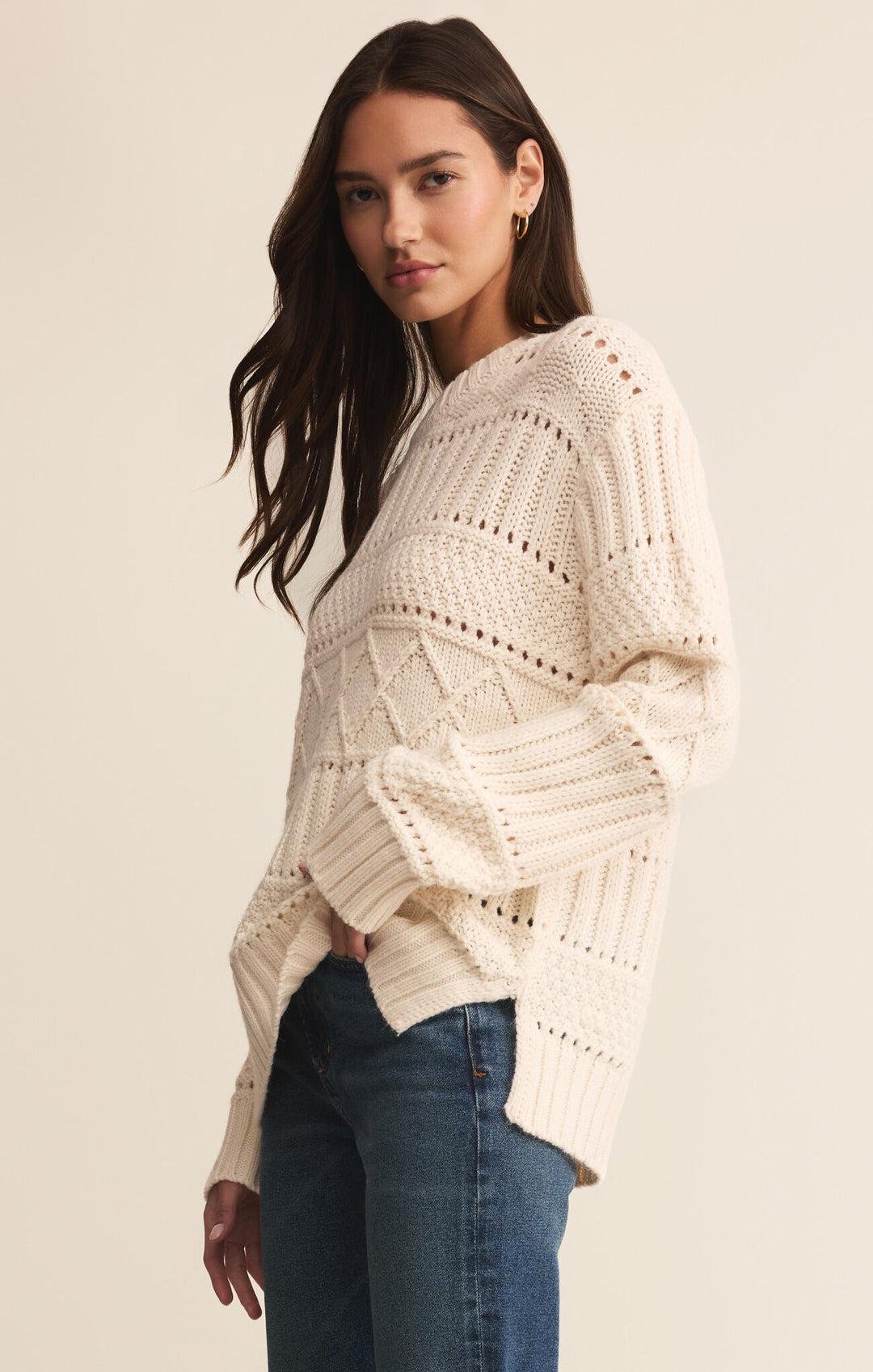 Woman wearing a cream knitted sweater and blue jeans on a beige background