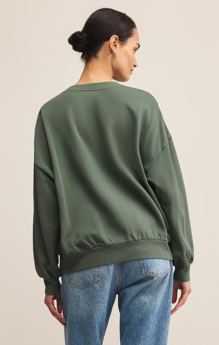 Person wearing a green sweatshirt and blue jeans on a beige background