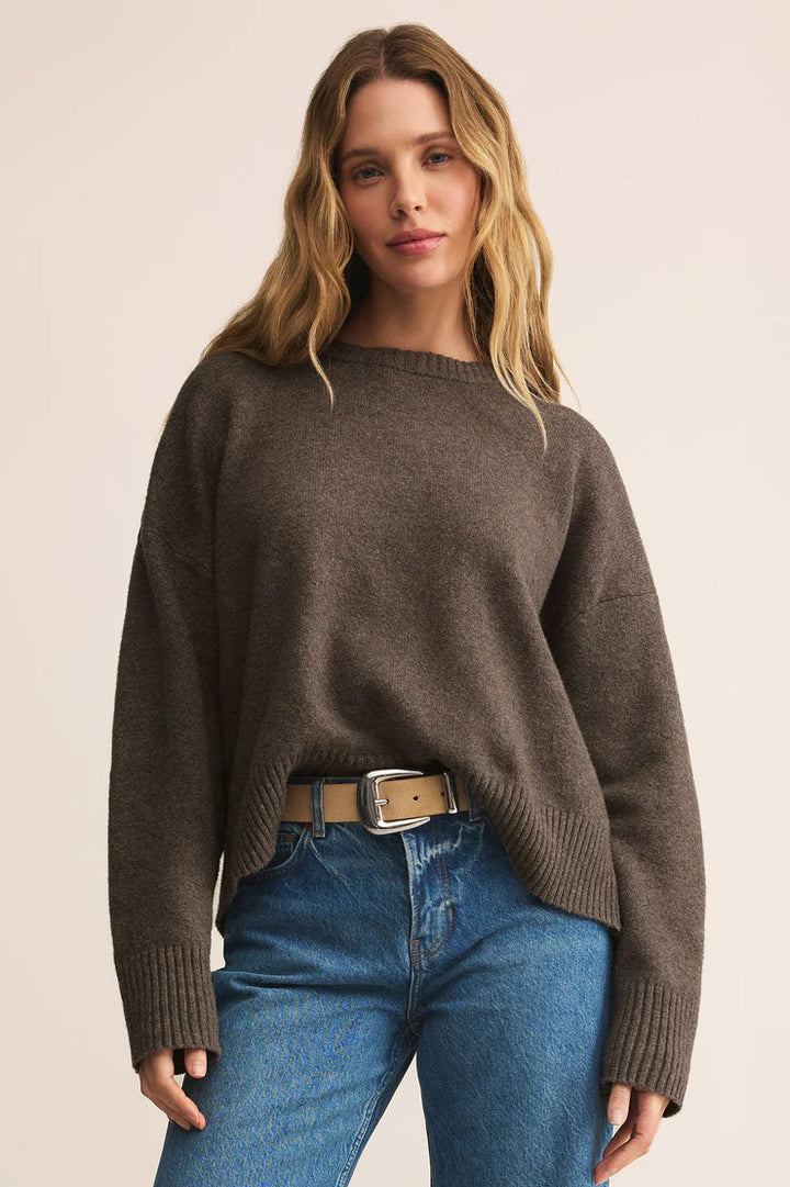 Woman wearing a brown sweater and blue jeans on a beige background