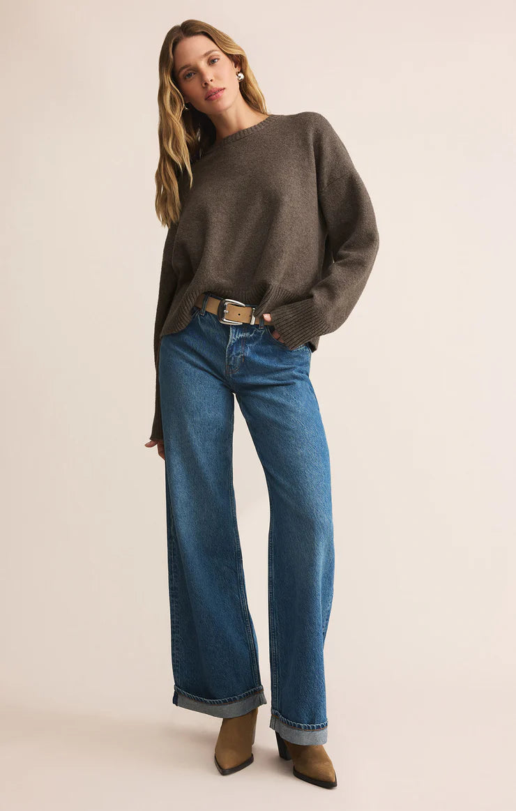 Woman wearing a brown sweater and blue jeans on a beige background