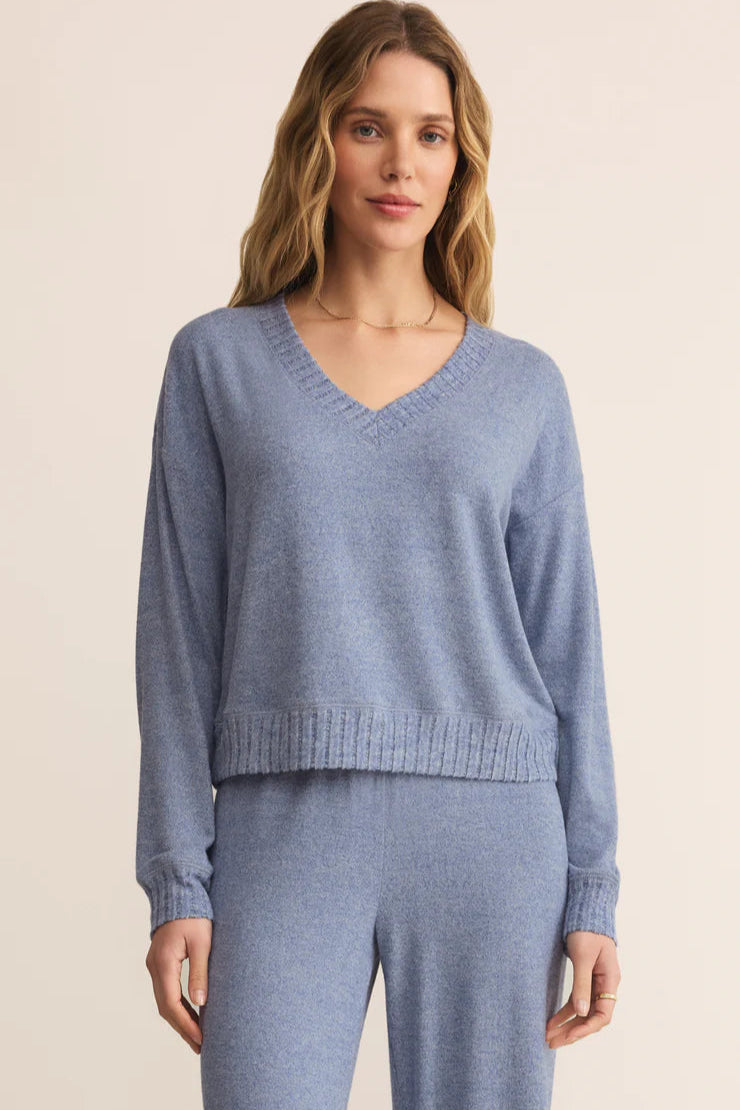 Woman wearing a blue silk jersey knit v neck top  and matching pants pants on a beige background
