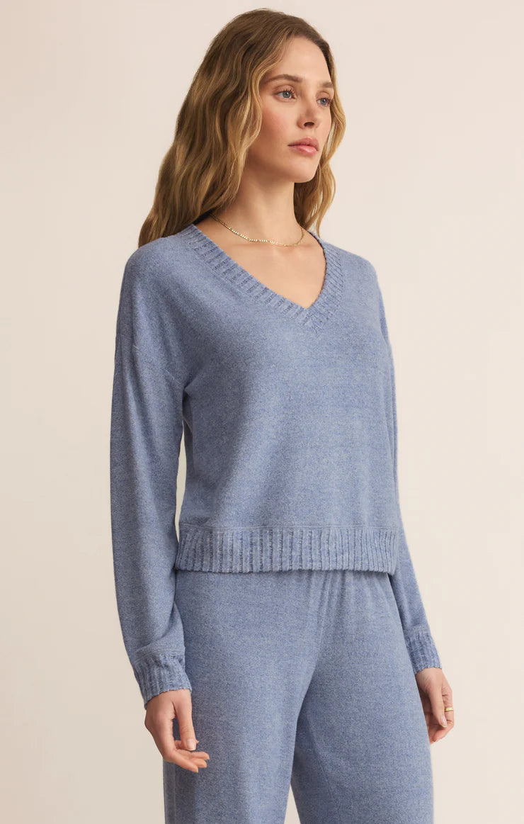Woman wearing a blue silk jersey knit v neck top  and matching pants pants on a beige background