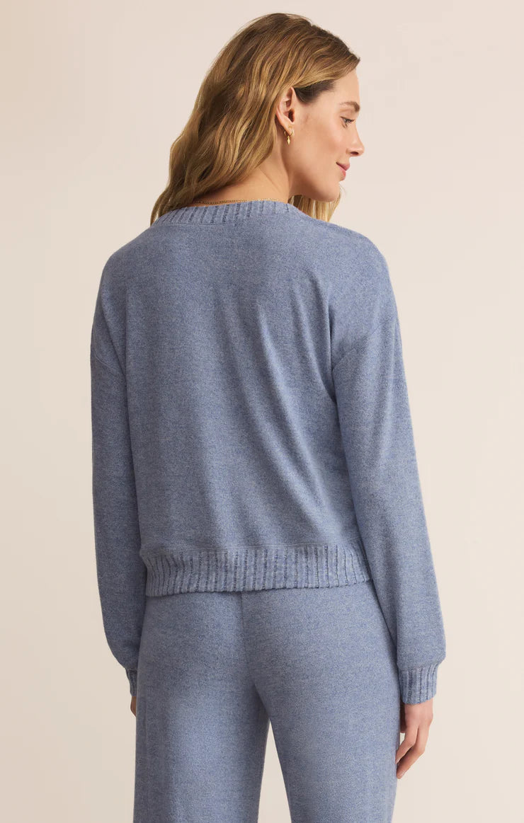 Woman wearing a blue silk jersey knit v neck top  and matching pants pants on a beige background