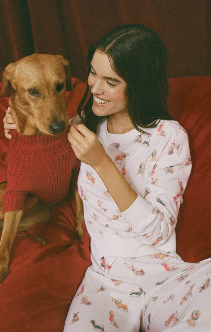 Woman in Z Supply white dog patterned pajamas sitting on a red couch with a dog wearing a red sweater.