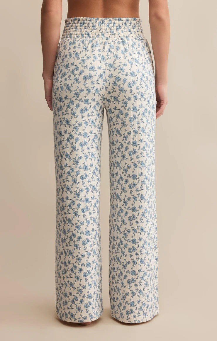 cream and blue floral-patterned pants worn by a person on a beige background