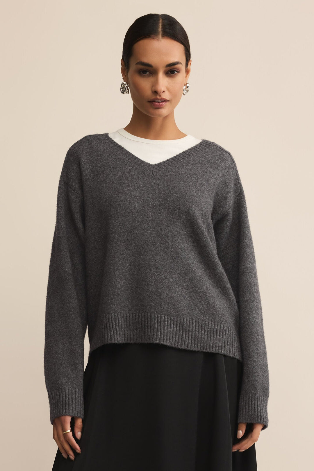 Woman wearing a gray sweater over a white shirt with a beige background