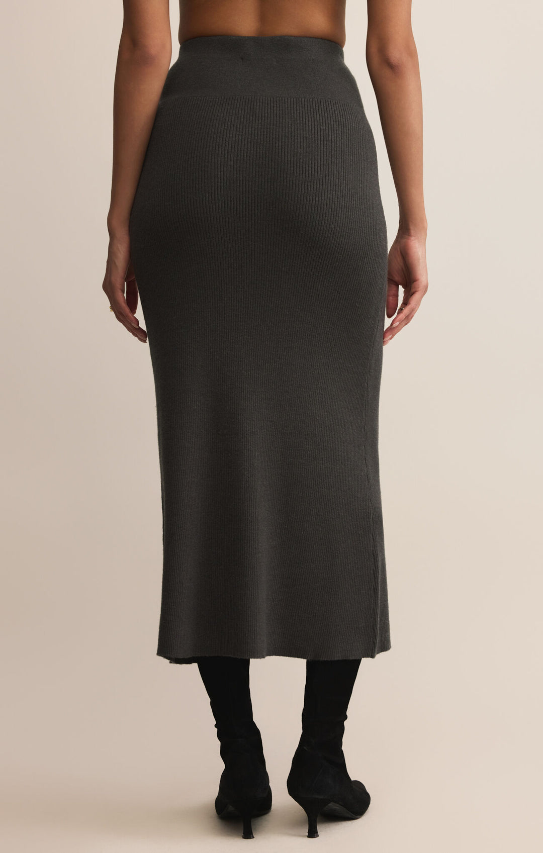 Person wearing a black ribbed skirt on a beige background