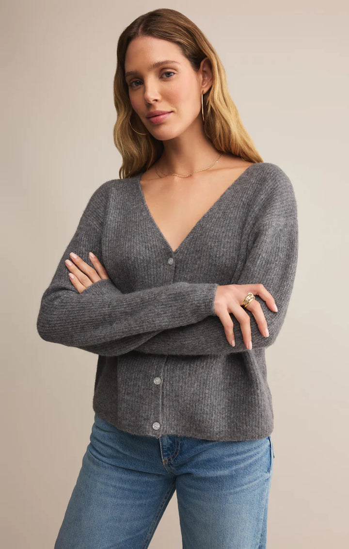 Woman wearing a gray sweater and blue jeans against a beige background